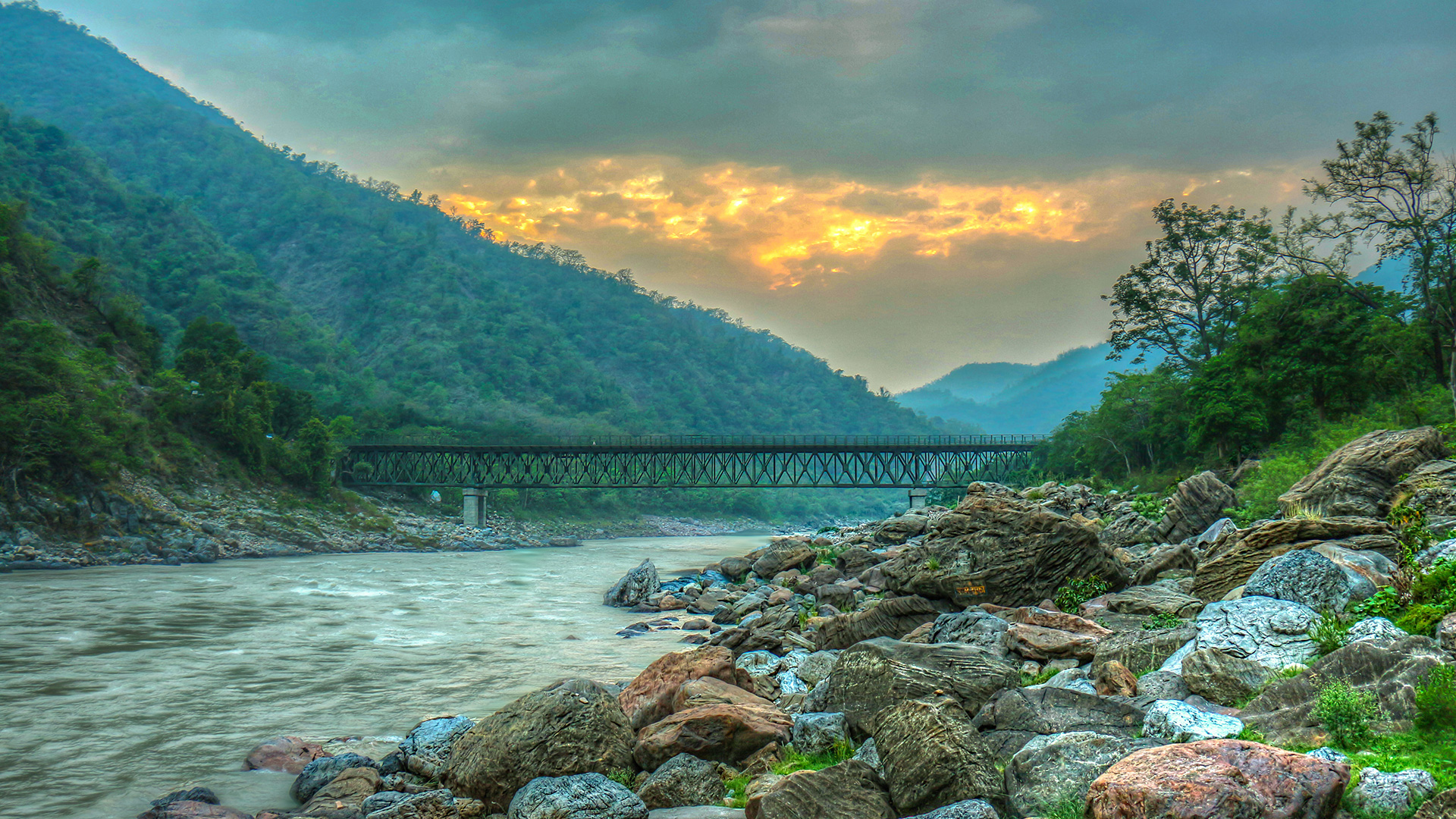 Mountain river flowing over rocks beneath a railway bridge at dusk